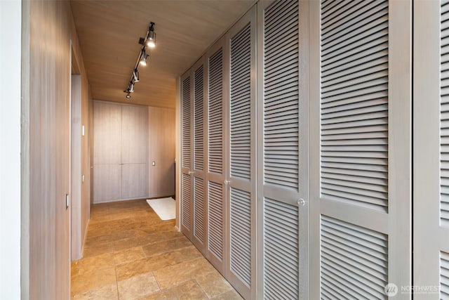 hallway featuring stone finish floor and rail lighting