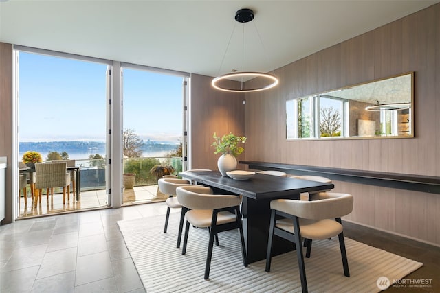 dining space featuring wood walls, a wall of windows, a water view, and light tile patterned flooring