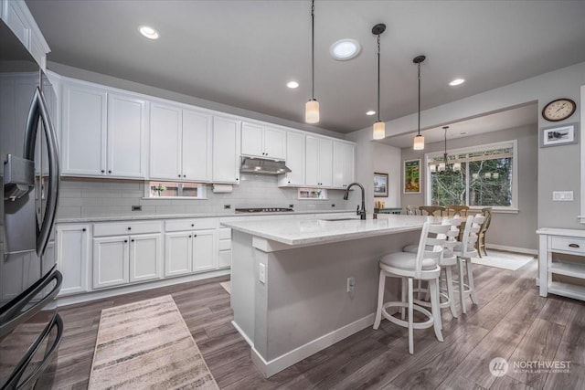 kitchen with white cabinets, decorative light fixtures, sink, a kitchen island with sink, and stainless steel refrigerator