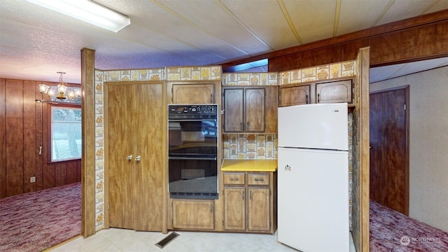 kitchen with hanging light fixtures, a notable chandelier, white refrigerator, wood walls, and black double oven