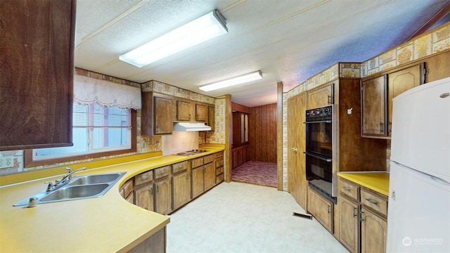 kitchen featuring a textured ceiling, white appliances, wood walls, and sink