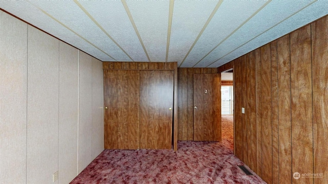 carpeted empty room featuring wooden walls