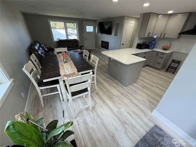 kitchen with gray cabinetry, a fireplace, wall chimney range hood, and light wood-type flooring