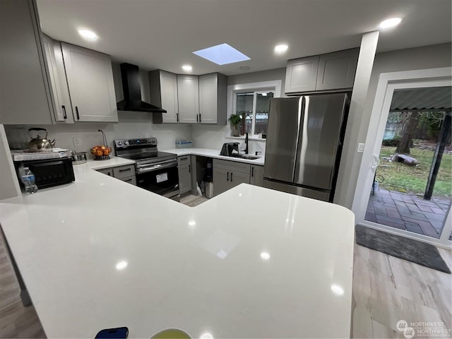 kitchen featuring a skylight, sink, wall chimney range hood, light hardwood / wood-style flooring, and appliances with stainless steel finishes