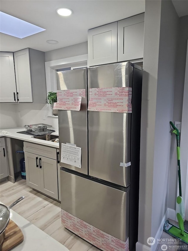 kitchen featuring a skylight, stainless steel fridge, light hardwood / wood-style flooring, and gray cabinets