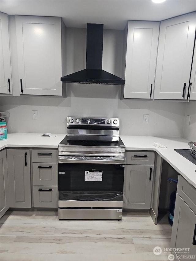 kitchen featuring stainless steel electric stove, wall chimney exhaust hood, light hardwood / wood-style floors, and gray cabinetry