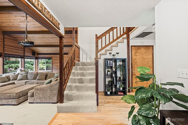 staircase featuring beam ceiling, wood-type flooring, and a textured ceiling