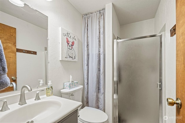 bathroom with a textured ceiling, vanity, toilet, and a shower with shower door