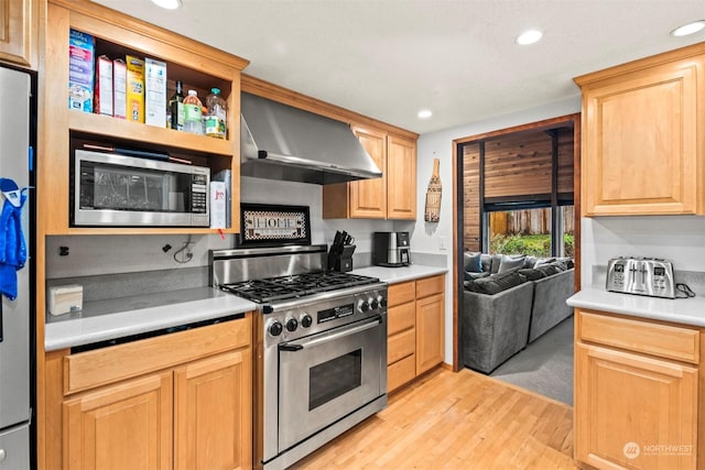 kitchen with light brown cabinets, light hardwood / wood-style floors, wall chimney range hood, and appliances with stainless steel finishes