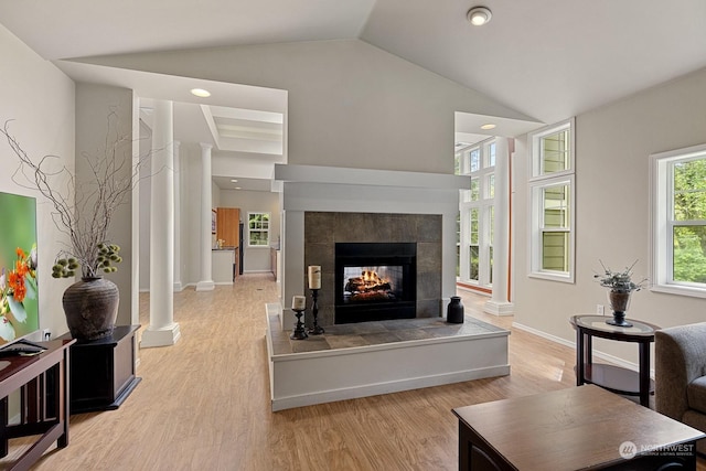 living room with a tiled fireplace, light hardwood / wood-style floors, vaulted ceiling, and ornate columns