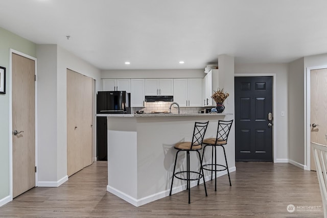 kitchen featuring white cabinets, refrigerator, decorative backsplash, light stone countertops, and a breakfast bar area