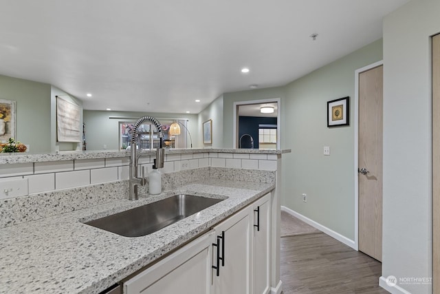 kitchen with hardwood / wood-style floors, light stone counters, white cabinetry, and sink