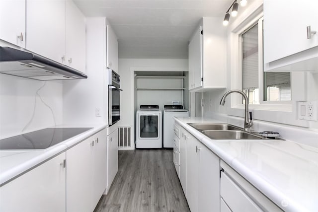 kitchen featuring electric cooktop, oven, sink, separate washer and dryer, and white cabinetry