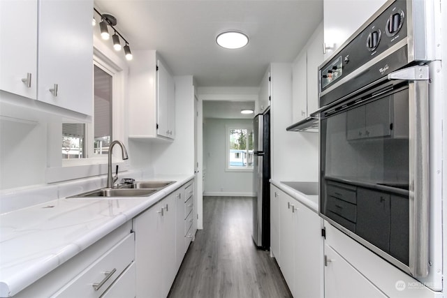 kitchen with white cabinetry, sink, light stone counters, light hardwood / wood-style floors, and black appliances