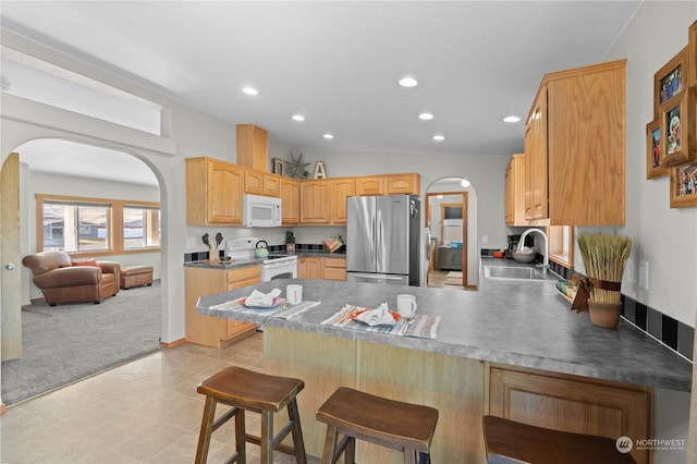 kitchen featuring light carpet, kitchen peninsula, a breakfast bar area, white appliances, and sink