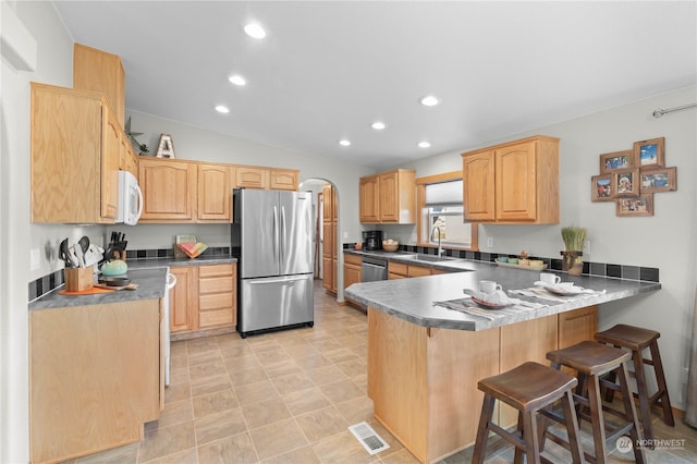 kitchen featuring lofted ceiling, light brown cabinets, stainless steel appliances, sink, and kitchen peninsula