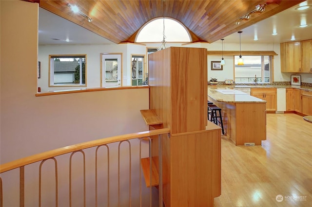 kitchen featuring light stone countertops, a center island, wooden ceiling, decorative light fixtures, and light brown cabinetry