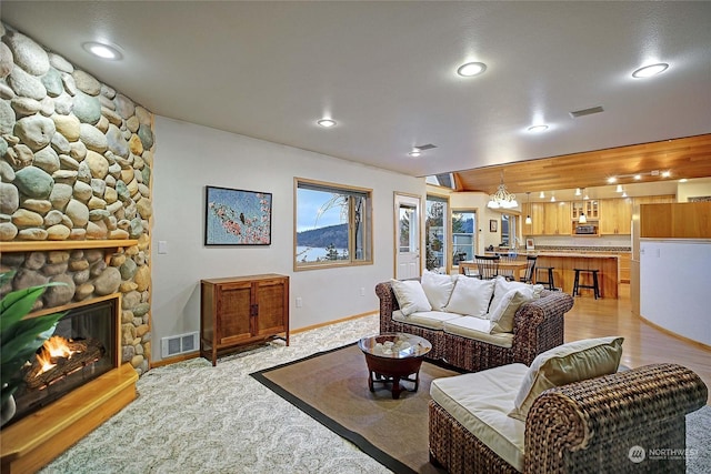 living room with a stone fireplace, a chandelier, and light wood-type flooring