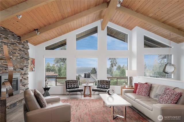 living area featuring vaulted ceiling with beams, wood finished floors, a stone fireplace, and wooden ceiling