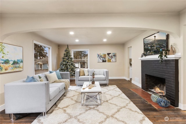 living room with crown molding, dark wood-type flooring, and a brick fireplace