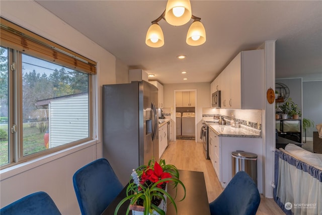 kitchen featuring separate washer and dryer, stainless steel appliances, hanging light fixtures, light stone countertops, and white cabinetry