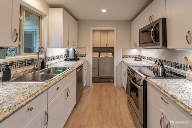 kitchen with independent washer and dryer, light hardwood / wood-style floors, white cabinetry, appliances with stainless steel finishes, and sink