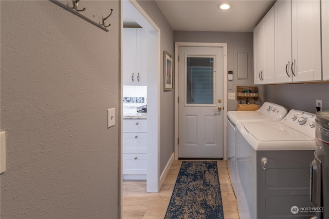 clothes washing area featuring washing machine and clothes dryer, cabinets, and light hardwood / wood-style flooring