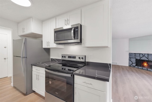 kitchen featuring white cabinets, a fireplace, stainless steel appliances, and light hardwood / wood-style flooring