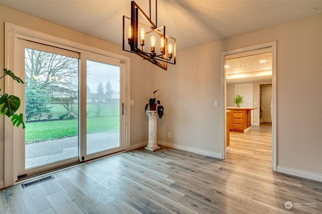 doorway to outside with a healthy amount of sunlight, light wood-type flooring, and a chandelier