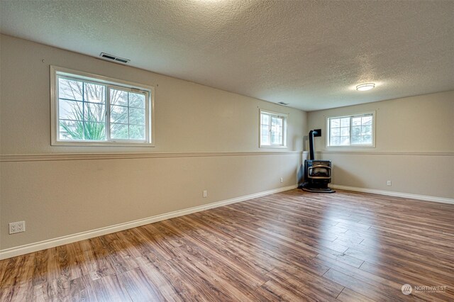 basement featuring a textured ceiling, hardwood / wood-style flooring, and a wood stove