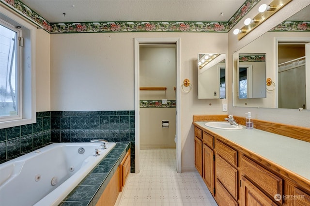 bathroom with vanity, toilet, plenty of natural light, and tiled bath