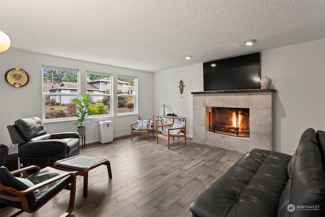 living room with wood-type flooring, a textured ceiling, and a tile fireplace