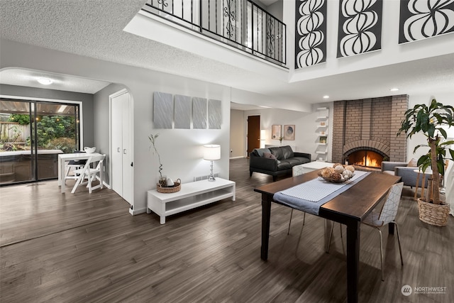 dining area featuring dark hardwood / wood-style floors, a towering ceiling, a textured ceiling, and a brick fireplace