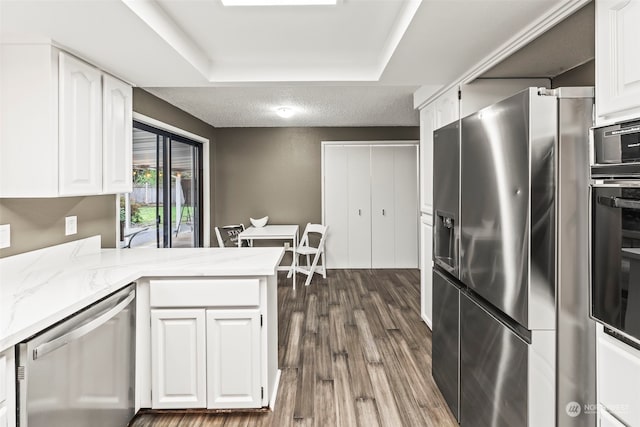 kitchen featuring a raised ceiling, dark hardwood / wood-style flooring, kitchen peninsula, white cabinets, and appliances with stainless steel finishes