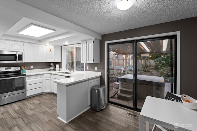 kitchen featuring white cabinetry, sink, stainless steel appliances, kitchen peninsula, and hardwood / wood-style floors