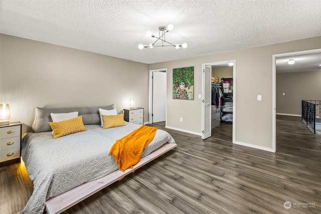 bedroom with an inviting chandelier, a walk in closet, a textured ceiling, dark hardwood / wood-style flooring, and a closet