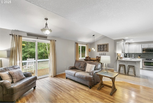 living room with a textured ceiling, light wood-type flooring, lofted ceiling, and sink