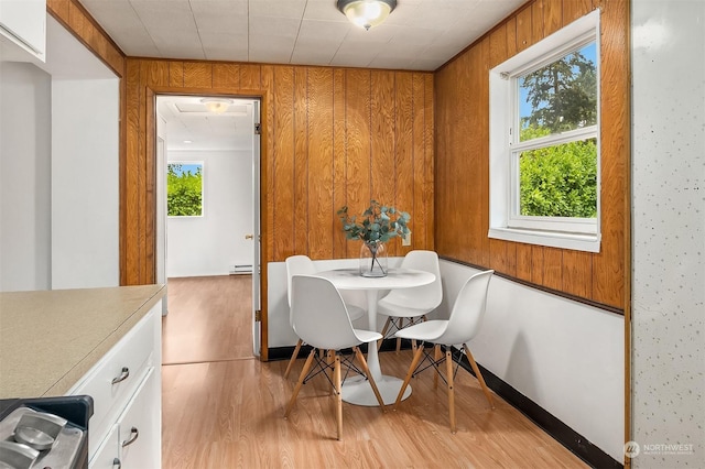 dining area with wood walls, light hardwood / wood-style floors, and a baseboard heating unit