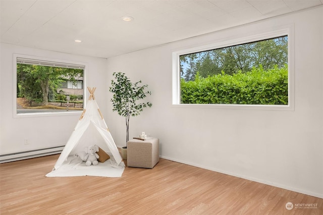 playroom featuring baseboard heating, a wealth of natural light, and light wood-type flooring