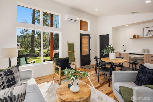 living area featuring a wall mounted air conditioner, a high ceiling, bar with sink, light wood-style flooring, and recessed lighting