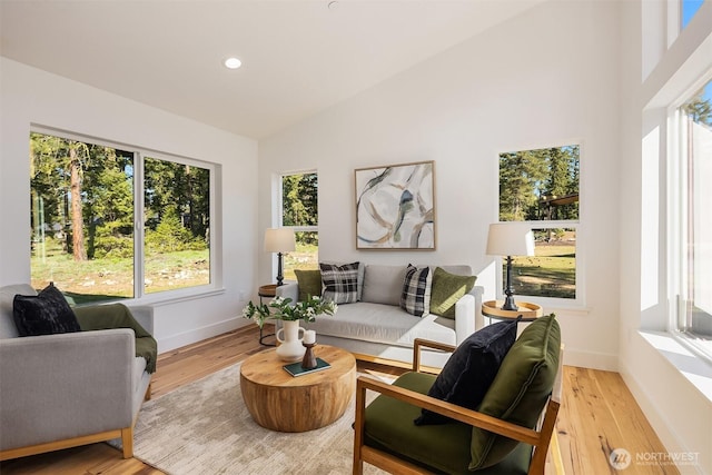 living area with plenty of natural light, high vaulted ceiling, light wood finished floors, baseboards, and recessed lighting