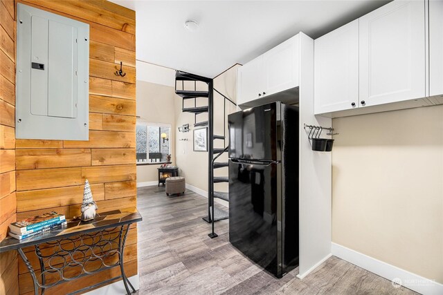 kitchen with black fridge, electric panel, light hardwood / wood-style floors, wooden walls, and white cabinets