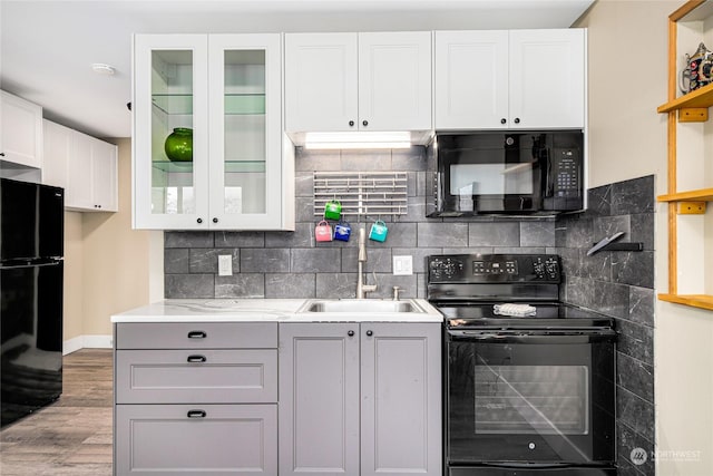 kitchen with light stone countertops, tasteful backsplash, sink, black appliances, and white cabinets