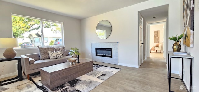 living area with light wood-style floors, baseboards, and a glass covered fireplace