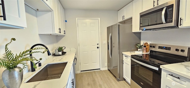 kitchen with light stone counters, a sink, white cabinetry, light wood-style floors, and appliances with stainless steel finishes