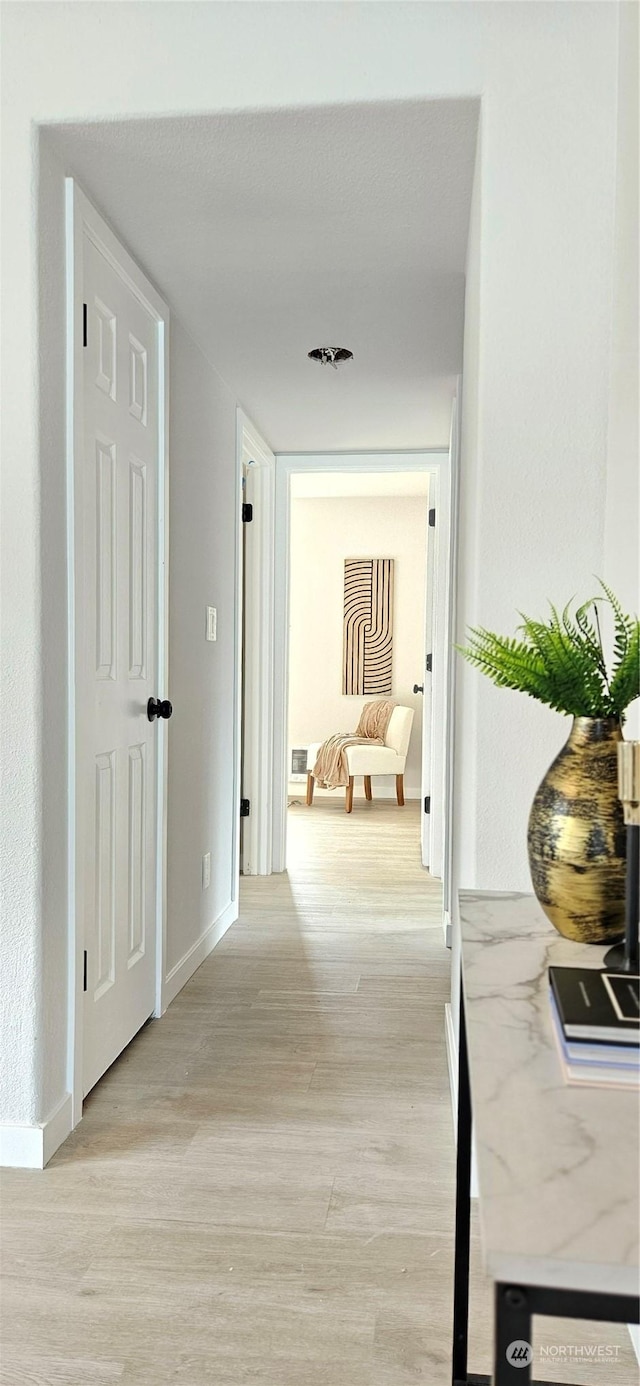 hallway featuring light wood-style flooring and baseboards