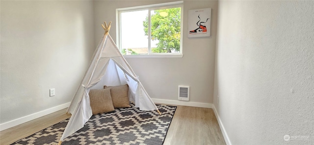 playroom featuring visible vents, a textured wall, baseboards, and wood finished floors