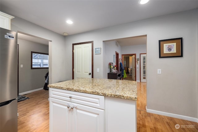 kitchen with white cabinets, stainless steel fridge, light stone counters, and light hardwood / wood-style flooring