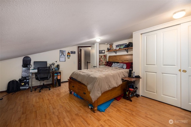 bedroom with a textured ceiling, light hardwood / wood-style floors, a closet, and lofted ceiling