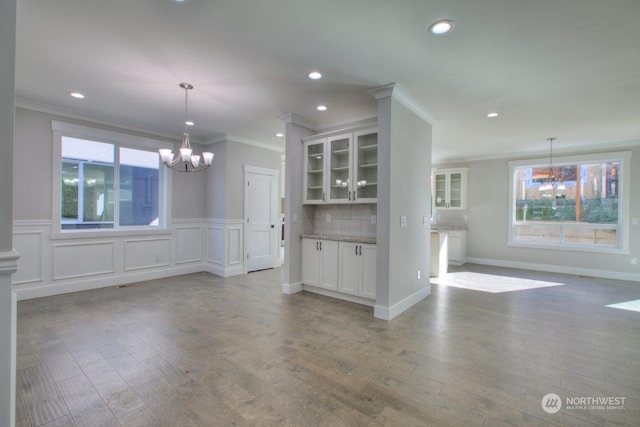 kitchen featuring a notable chandelier, white cabinets, ornamental molding, tasteful backsplash, and decorative light fixtures